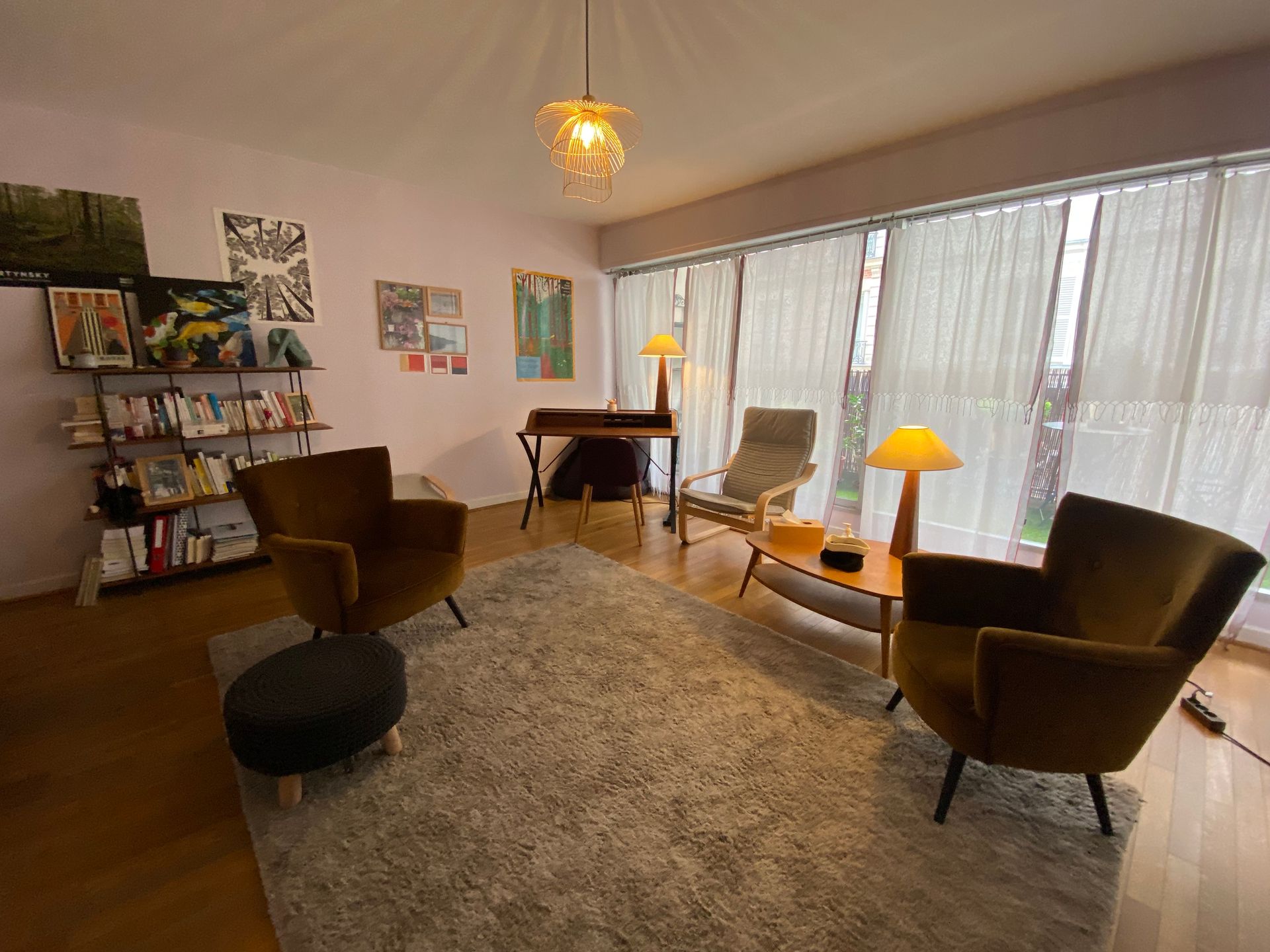 Salon confortable avec fauteuils marron, tapis beige, lampes et grandes fenêtres avec voilages.