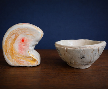 Deux bols en céramique, l'un blanc et orange en forme de croissant, l'autre petit bol beige, posés sur une surface en bois.