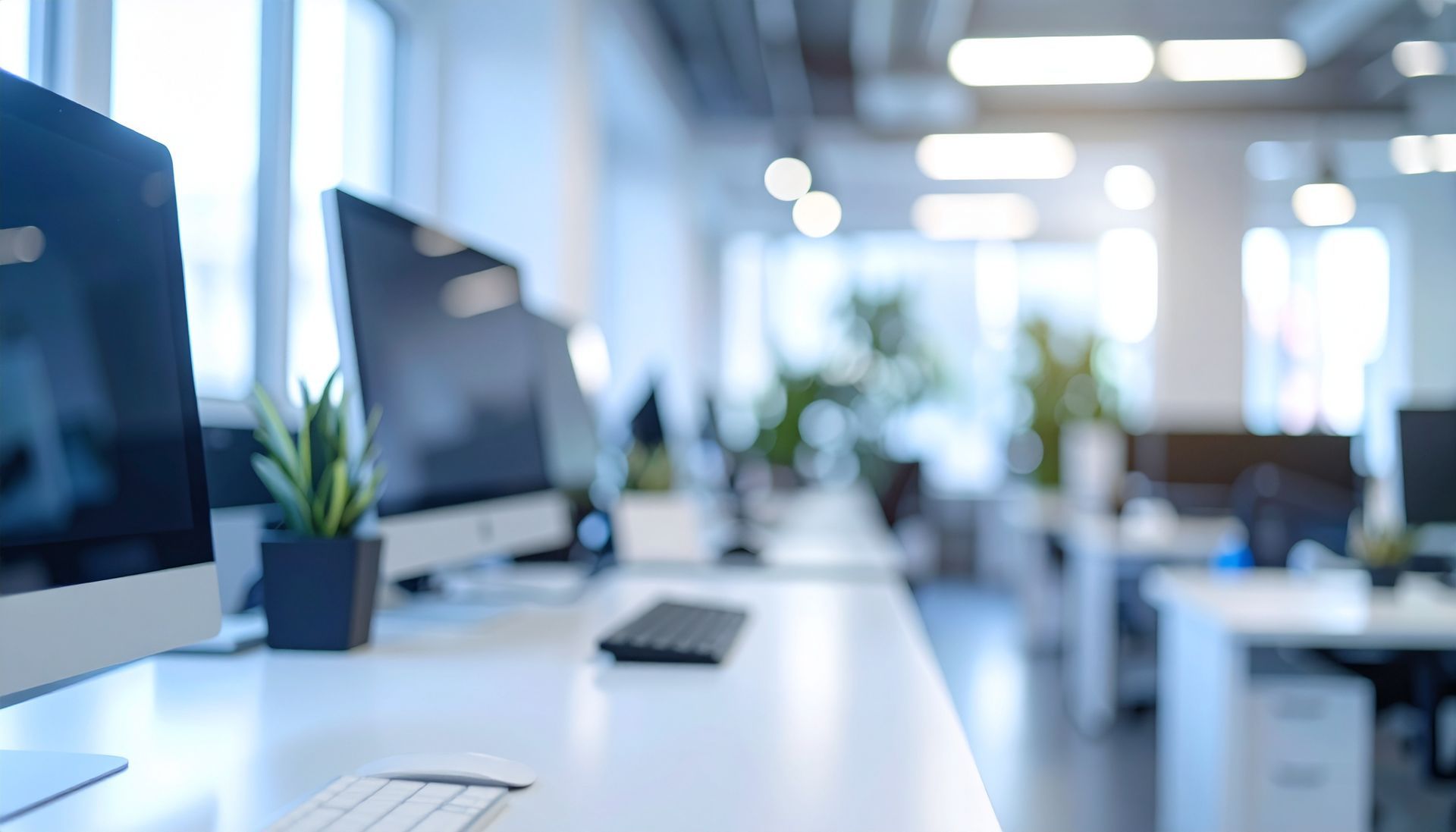Espace de bureau moderne avec bureaux blancs, ordinateurs et plantes en pot, arrière-plan flou.