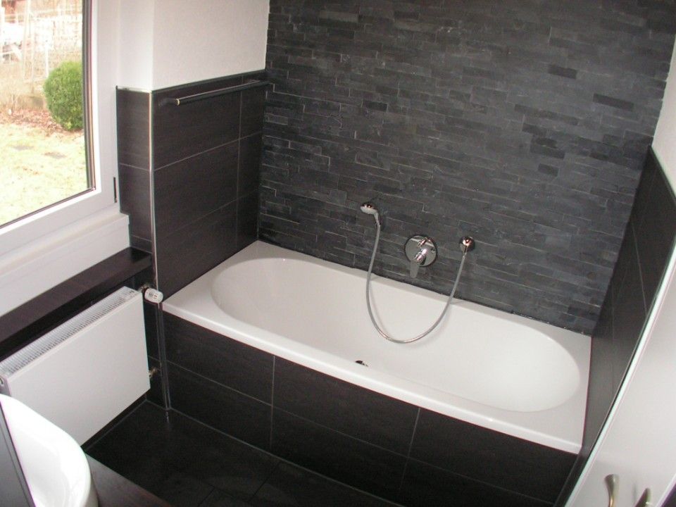 weiße Badewanne und schwarze Fliesen an einer Wand