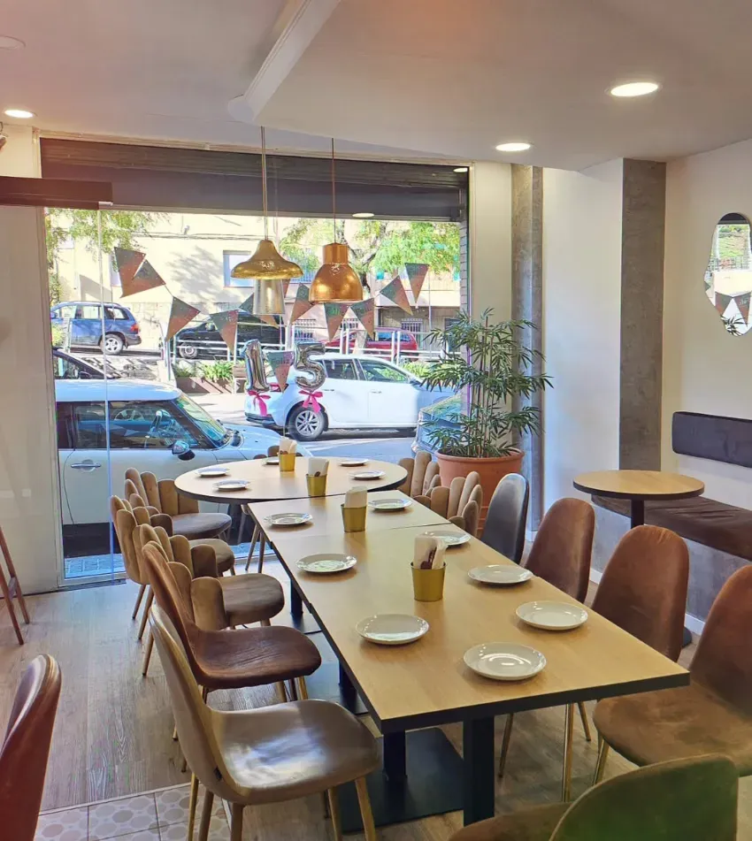 Comedor de cafetería moderno con una larga mesa de madera, sillas marrones y grandes ventanales que dan a la calle.