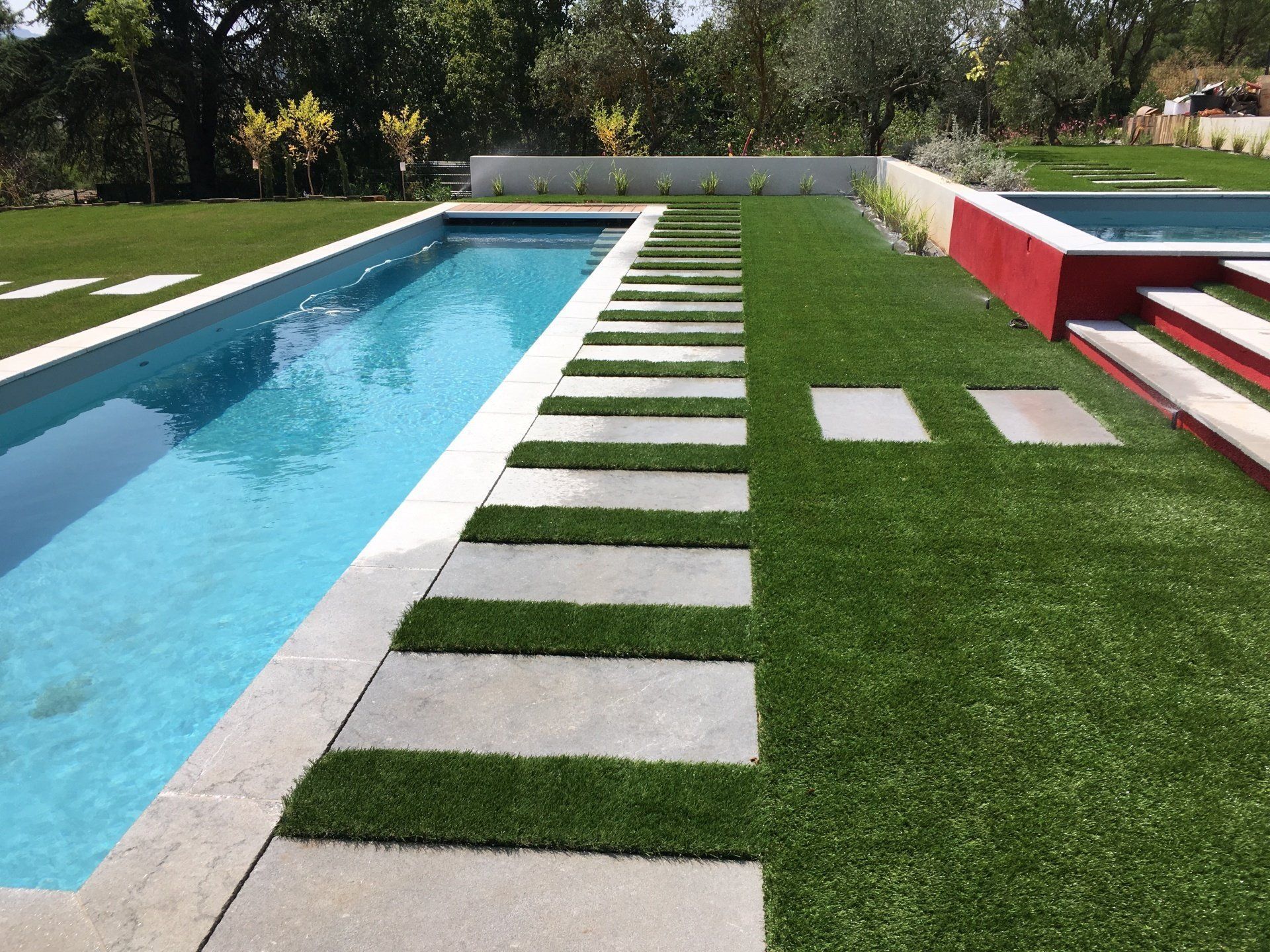 Piscine en longueur avec pelouse et chemin de dalles au bord