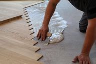 Un hombre está aplicando pegamento a un piso de madera con una espátula.