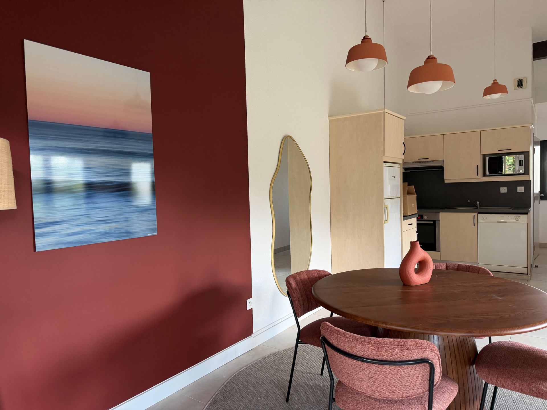 Salle à manger moderne avec un mur d'accent rouge, une table ronde en bois, des chaises roses et une cuisine ouverte