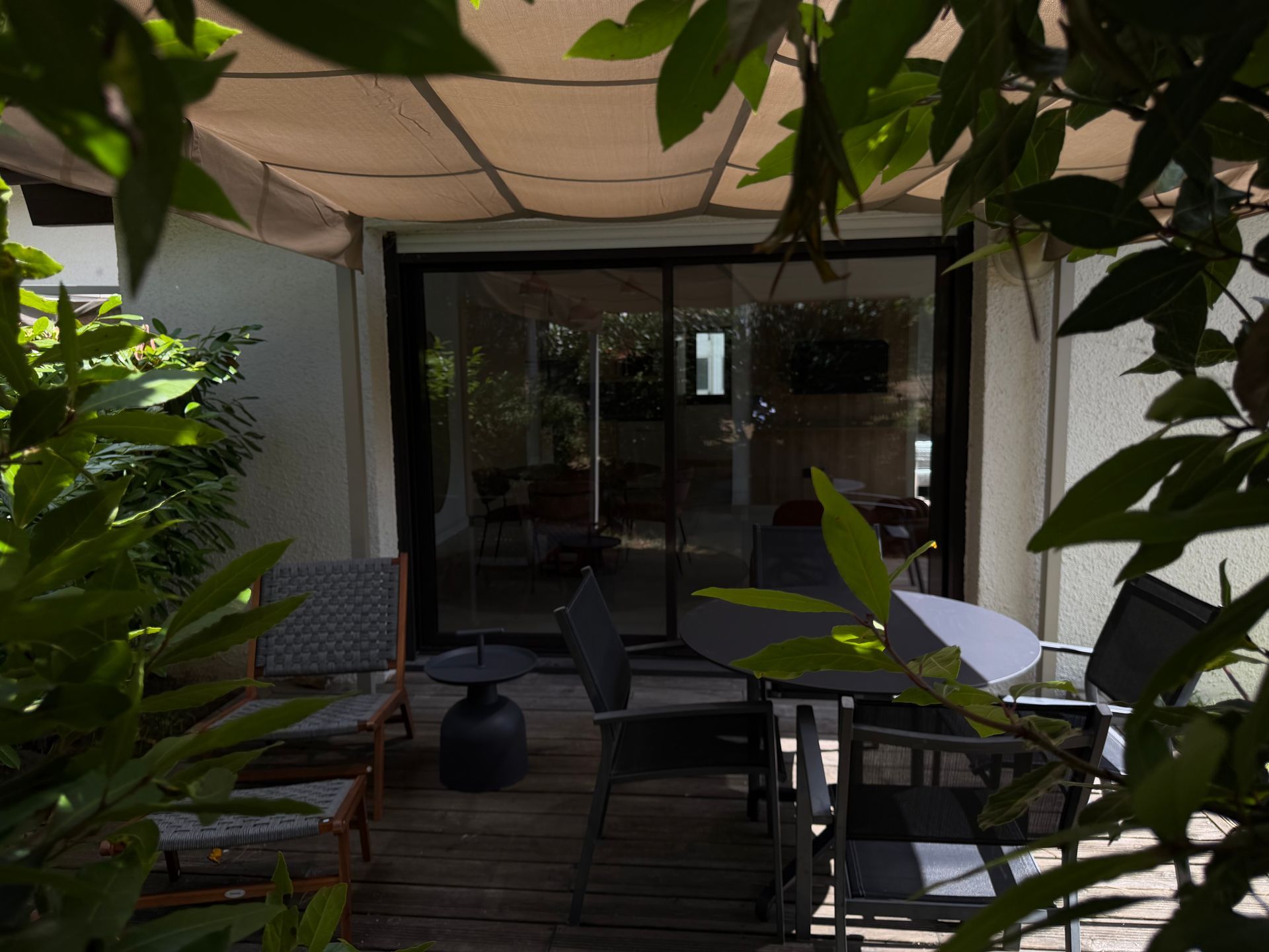 Patio couvert avec terrasse en bois, chaises, table et plantes en pot près des portes vitrées