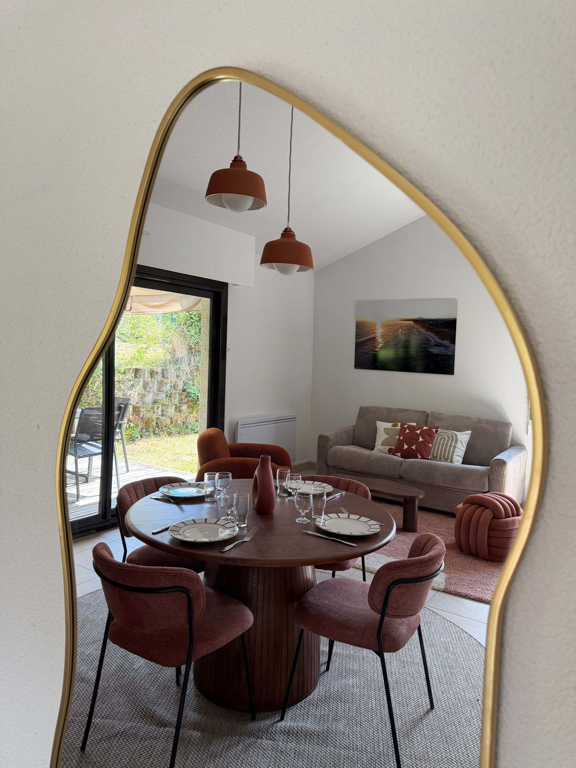 Coin repas avec table ronde en bois, chaises couleur rouille, suspensions lumineuses et canapé dans un salon lumineux