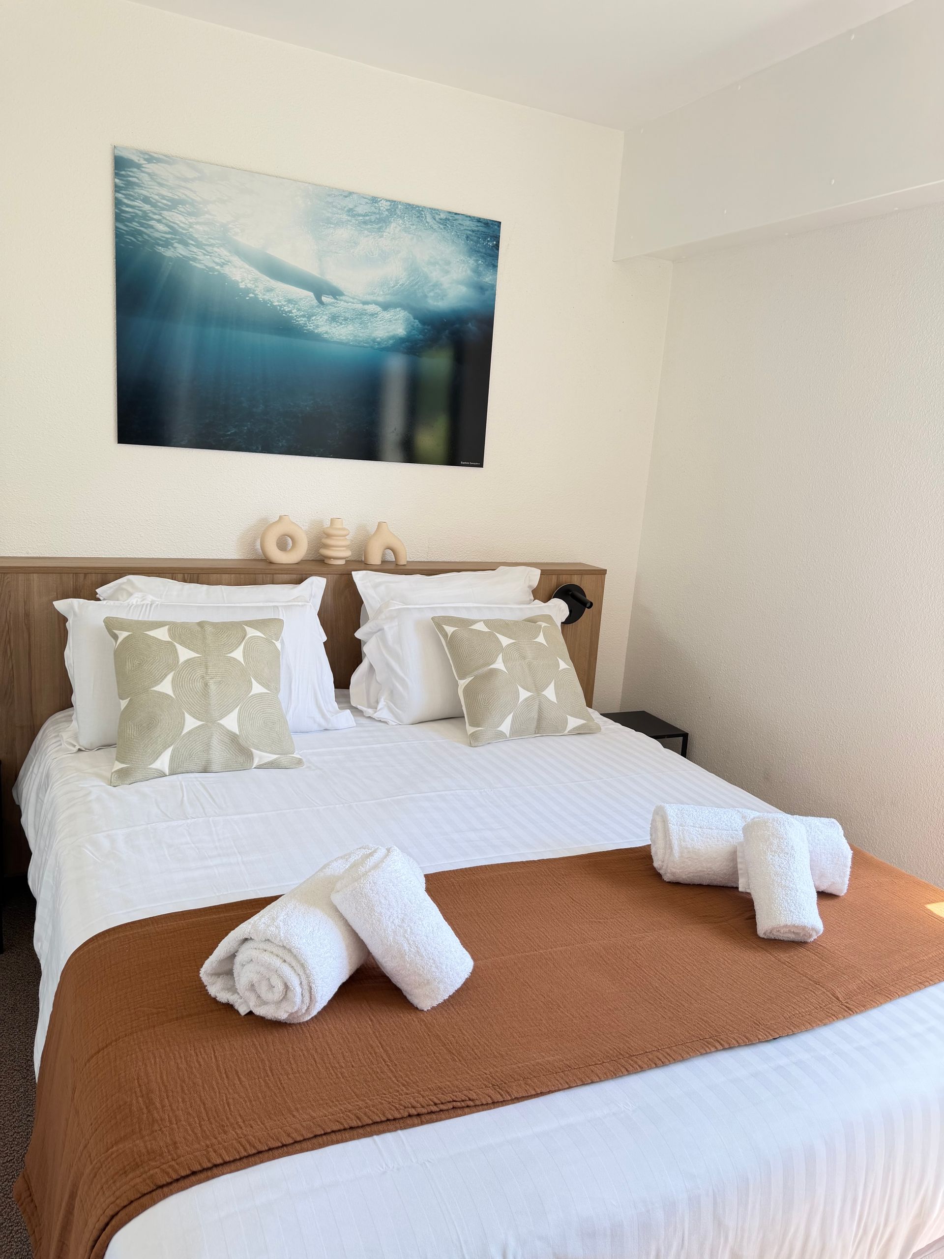 Chambre confortable avec un lit bien fait, des draps blancs, un jeté beige et une décoration murale.