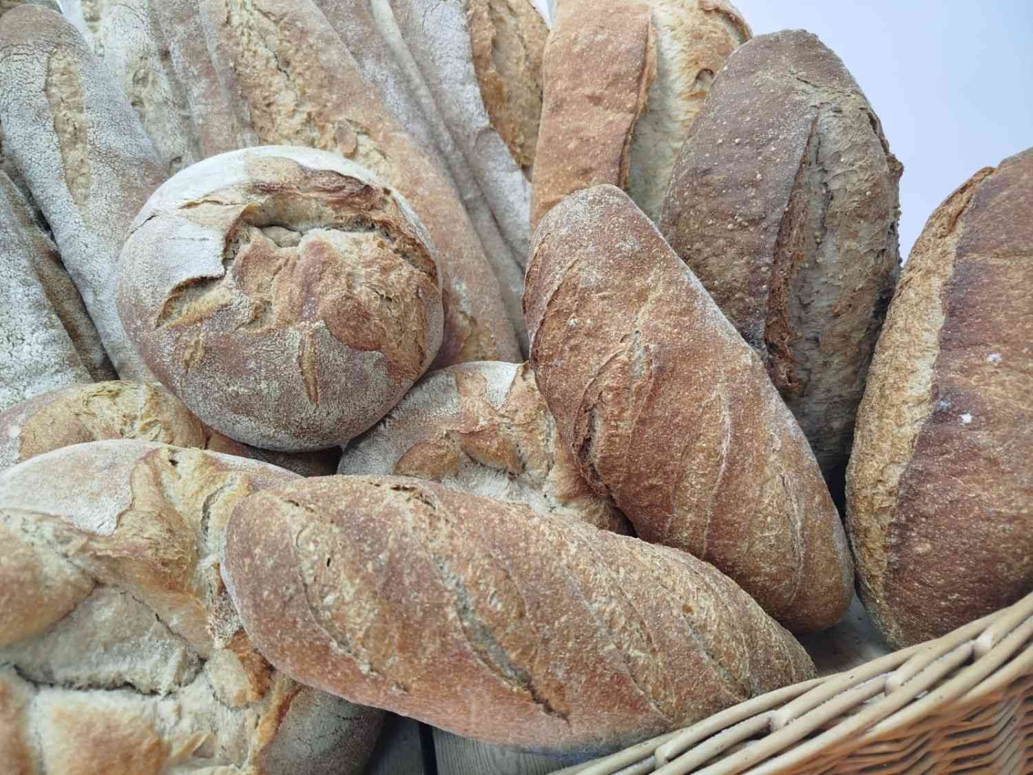 Una cesta repleta de una variedad de panes artesanales de corteza crujiente, de color marrón dorado.