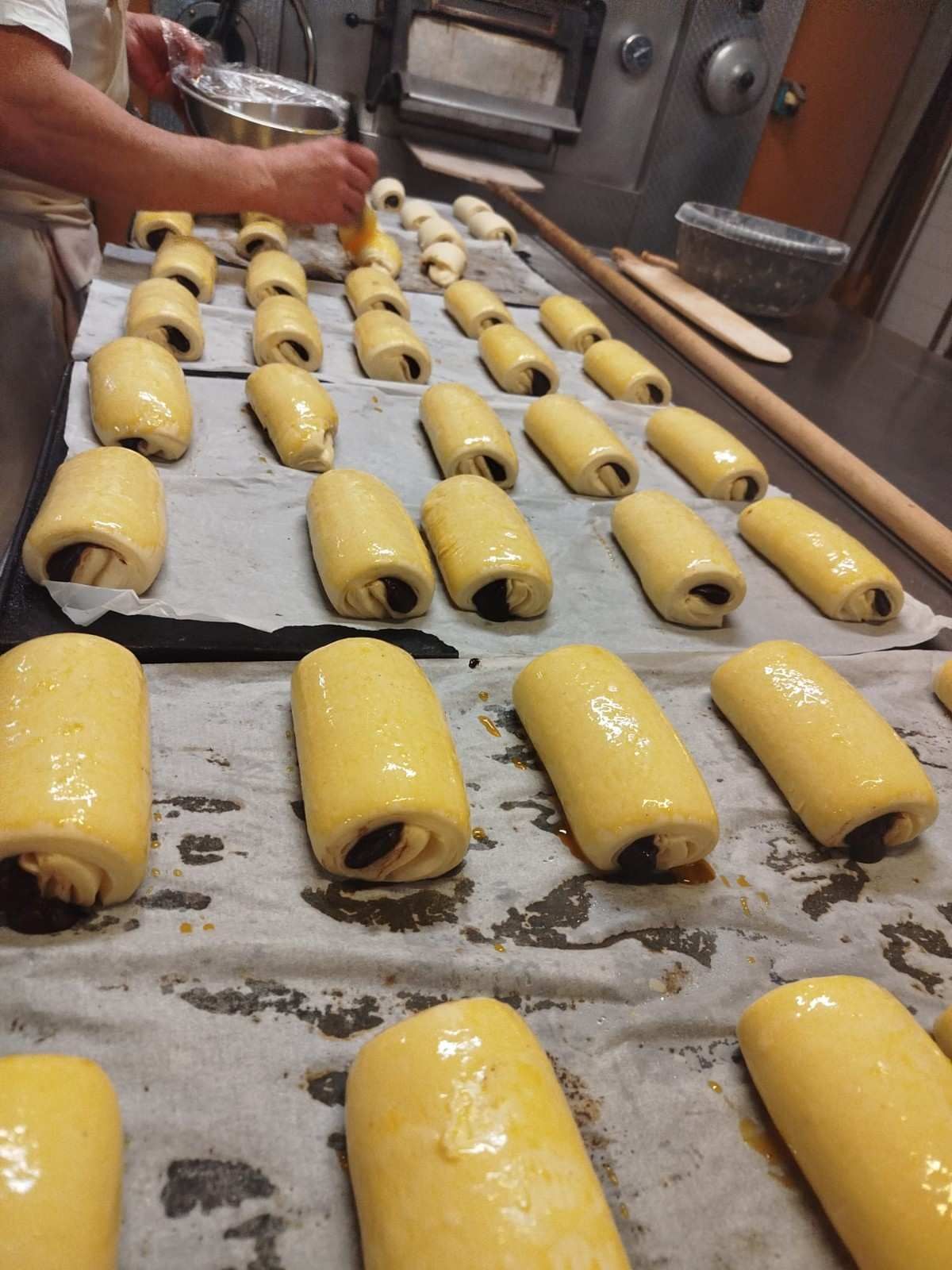 En una cocina, un panadero pinta con huevo batido hileras de pasteles rellenos de chocolate sin hornear.