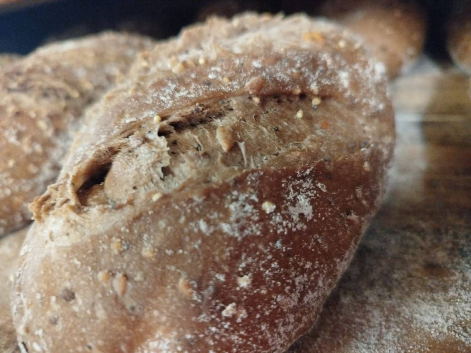 Primer plano de una hogaza de pan crujiente, de color marrón oscuro, con semillas y una hendidura en la parte superior.