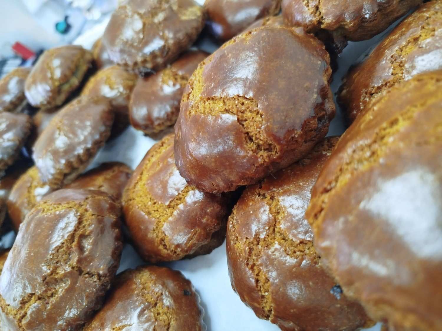Un montón de galletas recién horneadas, brillantes y glaseadas de color marrón sobre una superficie blanca.