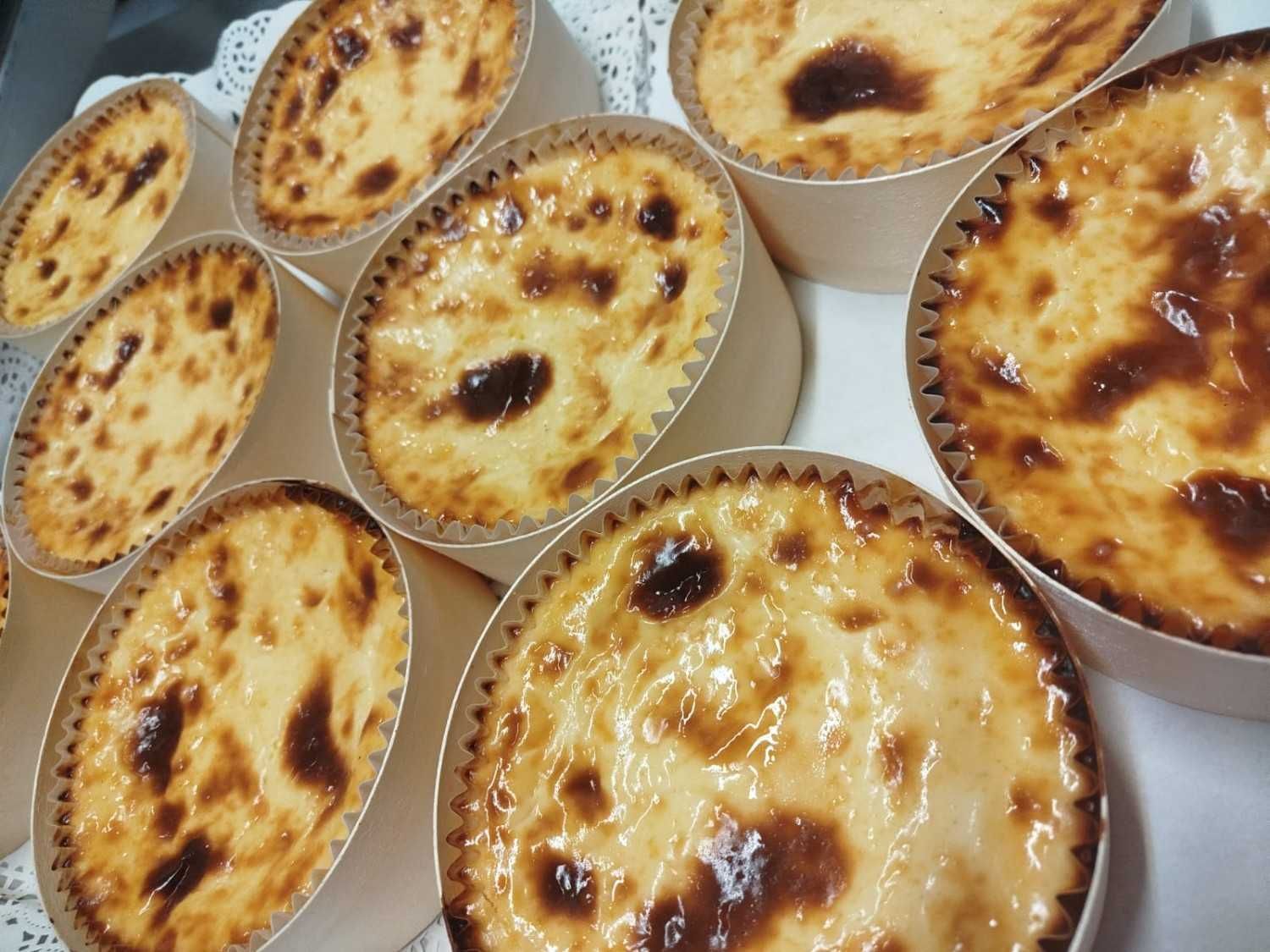 Un grupo de pequeñas tartaletas de crema pastelera horneadas, de color marrón dorado, dispuestas en moldes de papel.
