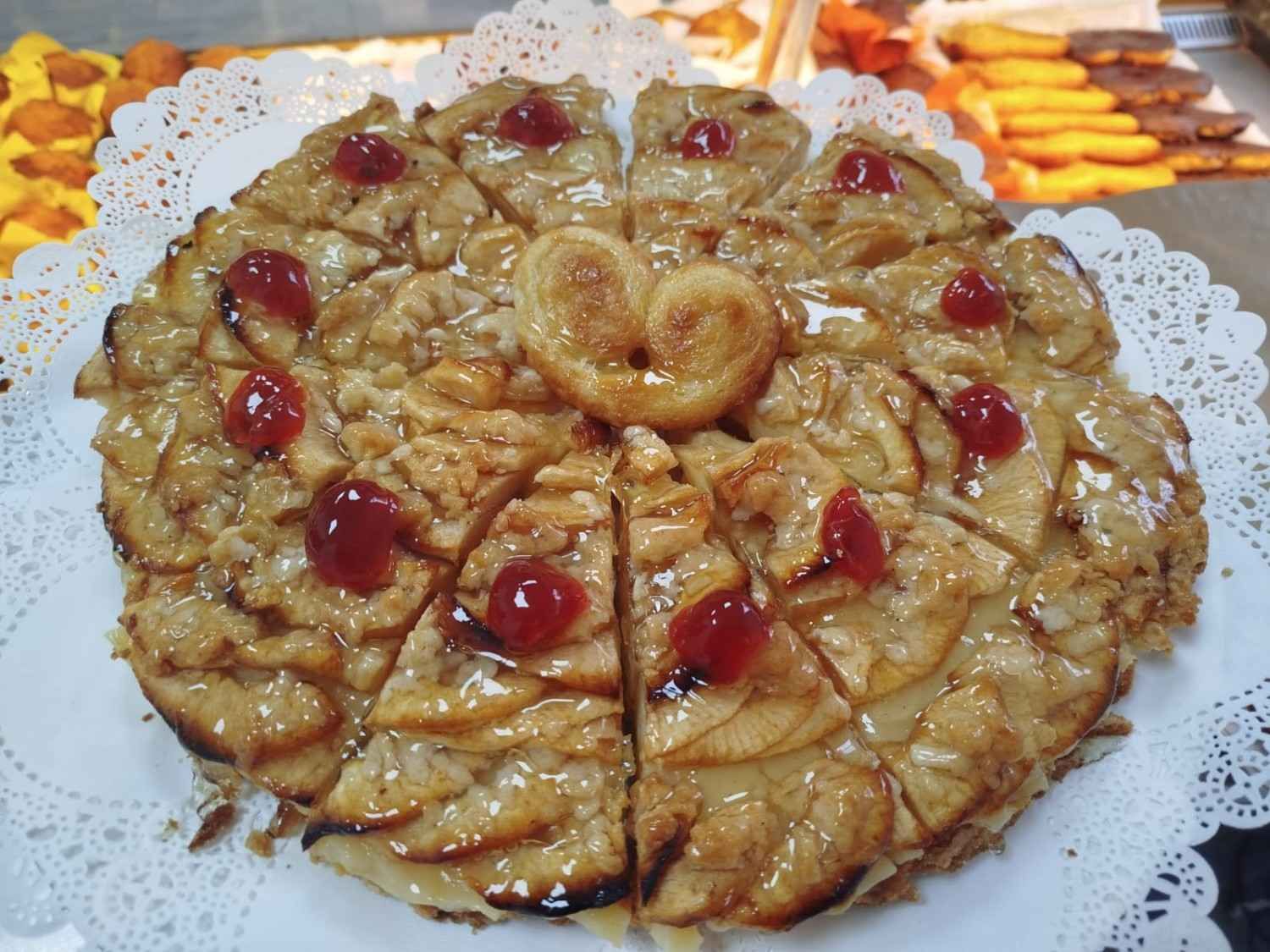 Una tarta de manzana en rodajas decorada con cerezas rojas confitadas y un corazón de hojaldre.