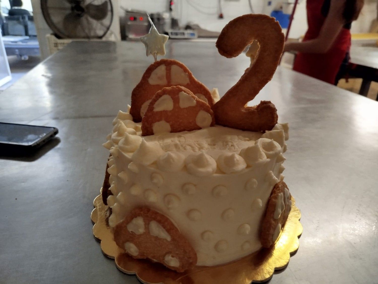 Una tarta redonda de cumpleaños glaseada, coronada con una galleta con forma del número 2.