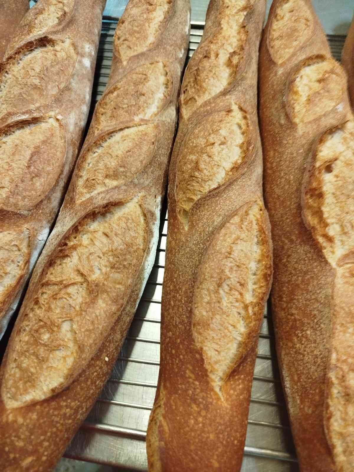 Varias baguettes recién horneadas, doradas y con la parte superior marcada, reposan sobre una rejilla.