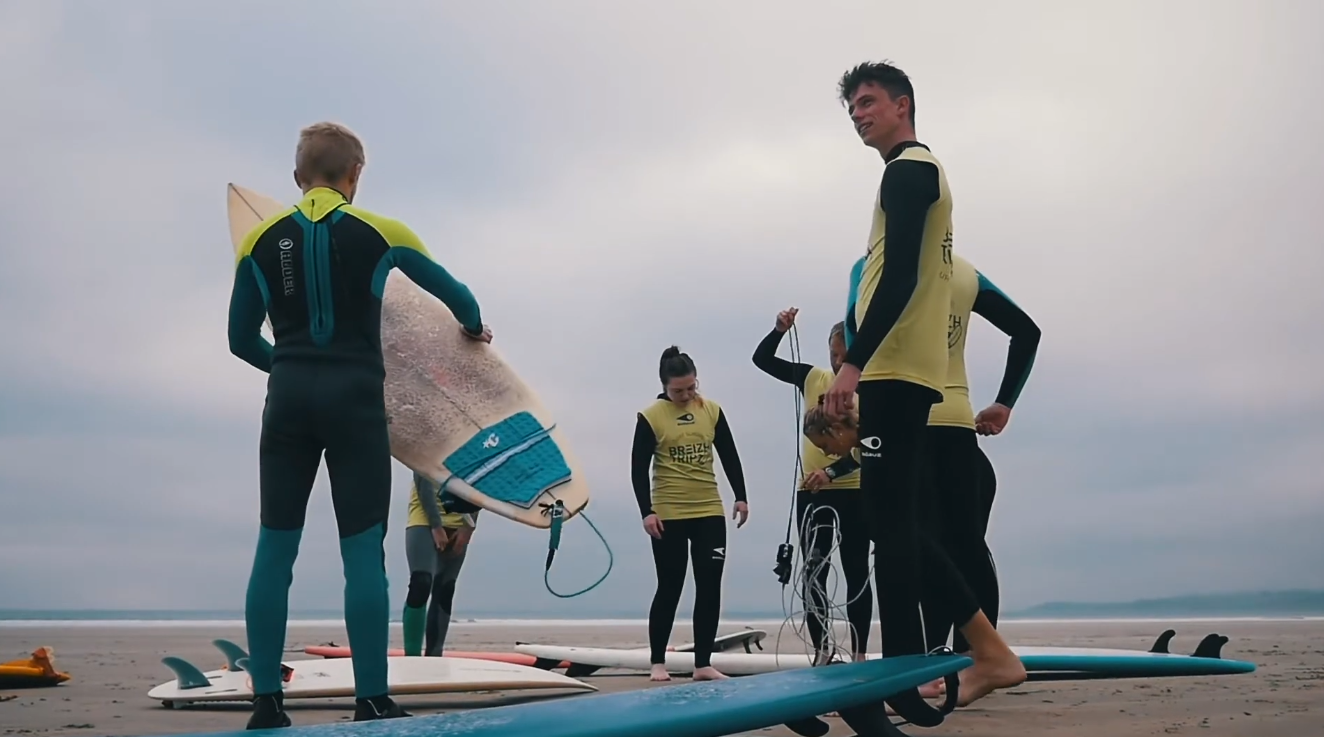 Des surfeurs en combinaison se tiennent sur leurs planches près du rivage, prêts à pagayer vers le large.