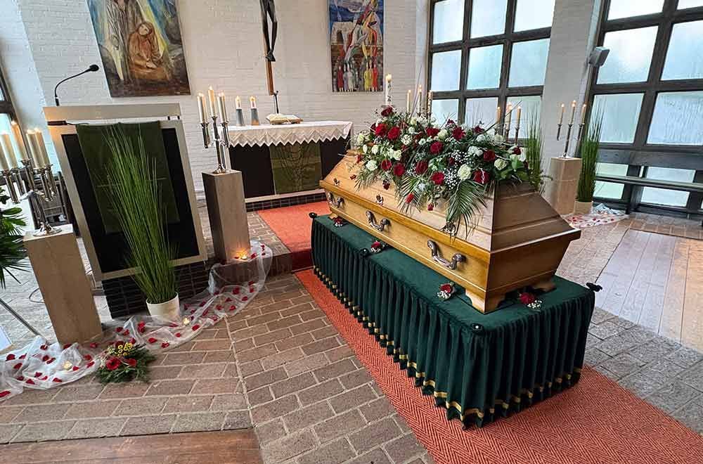 Ein mit Blumen geschmückter Holzsarg in einer Kirche, vorbereitet für eine Trauerfeier.