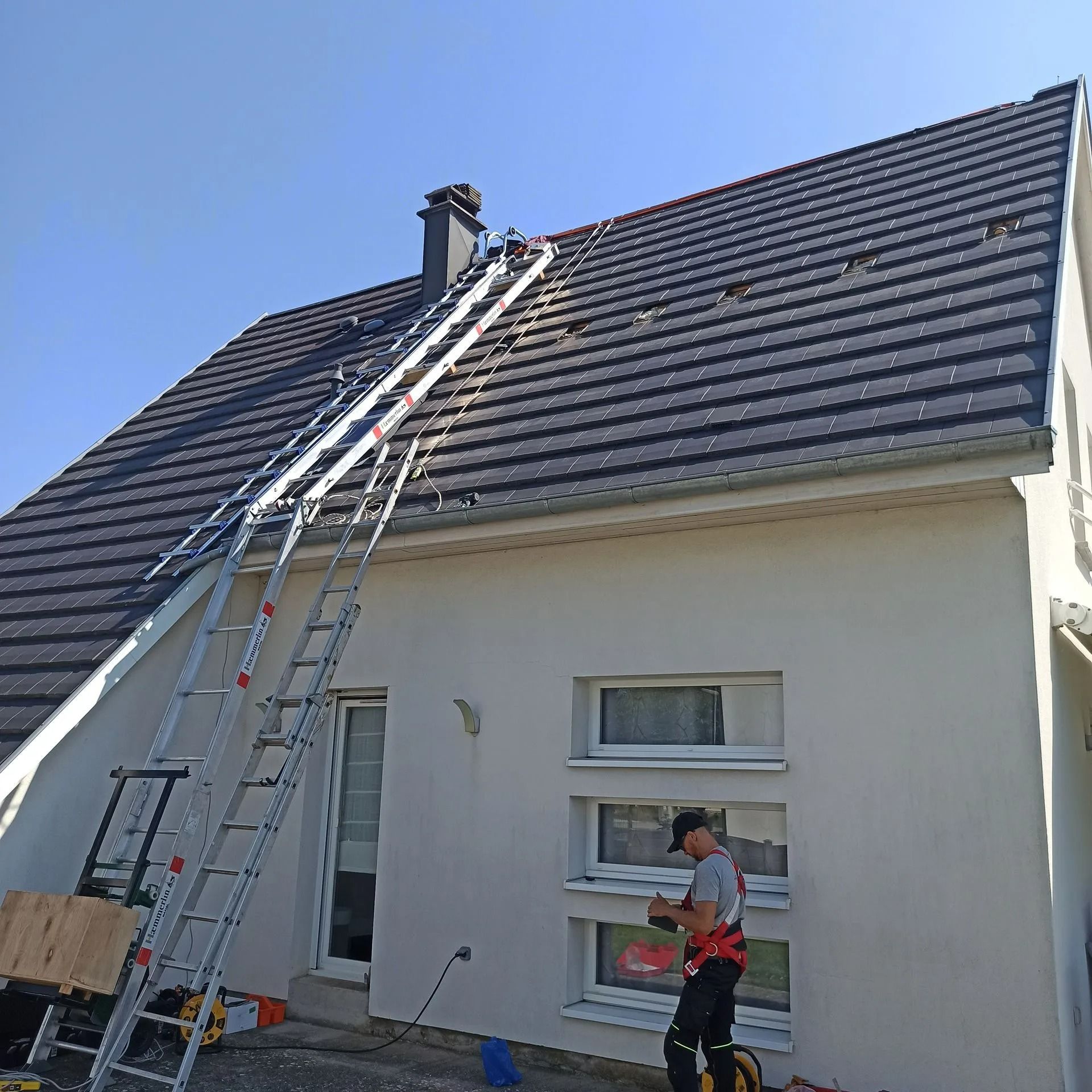 Une personne sur un toit avec une échelle, travaillant sur une maison au toit sombre et au bardage clair.