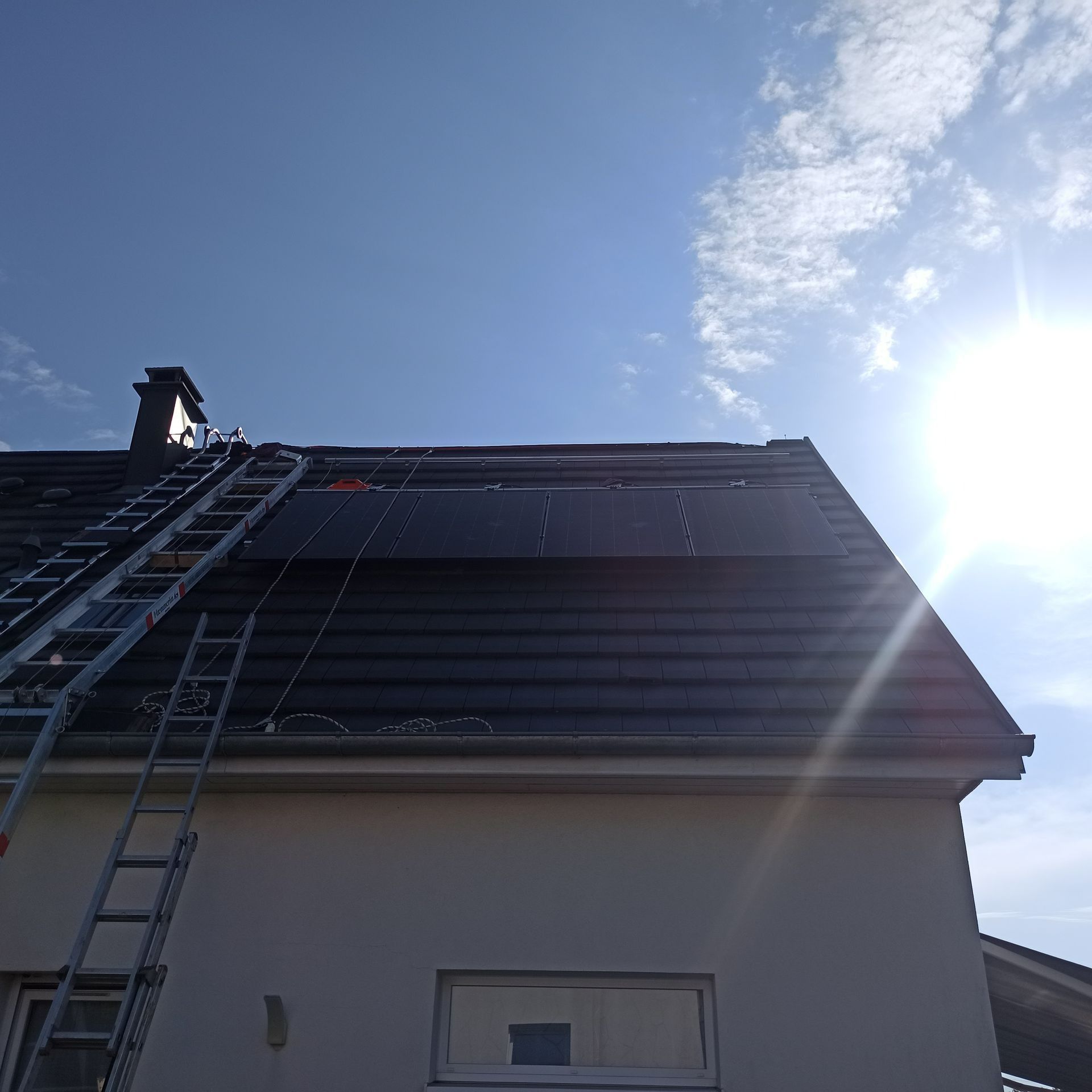 Un toit de maison avec des panneaux photovoltaïques installés et une échelle.