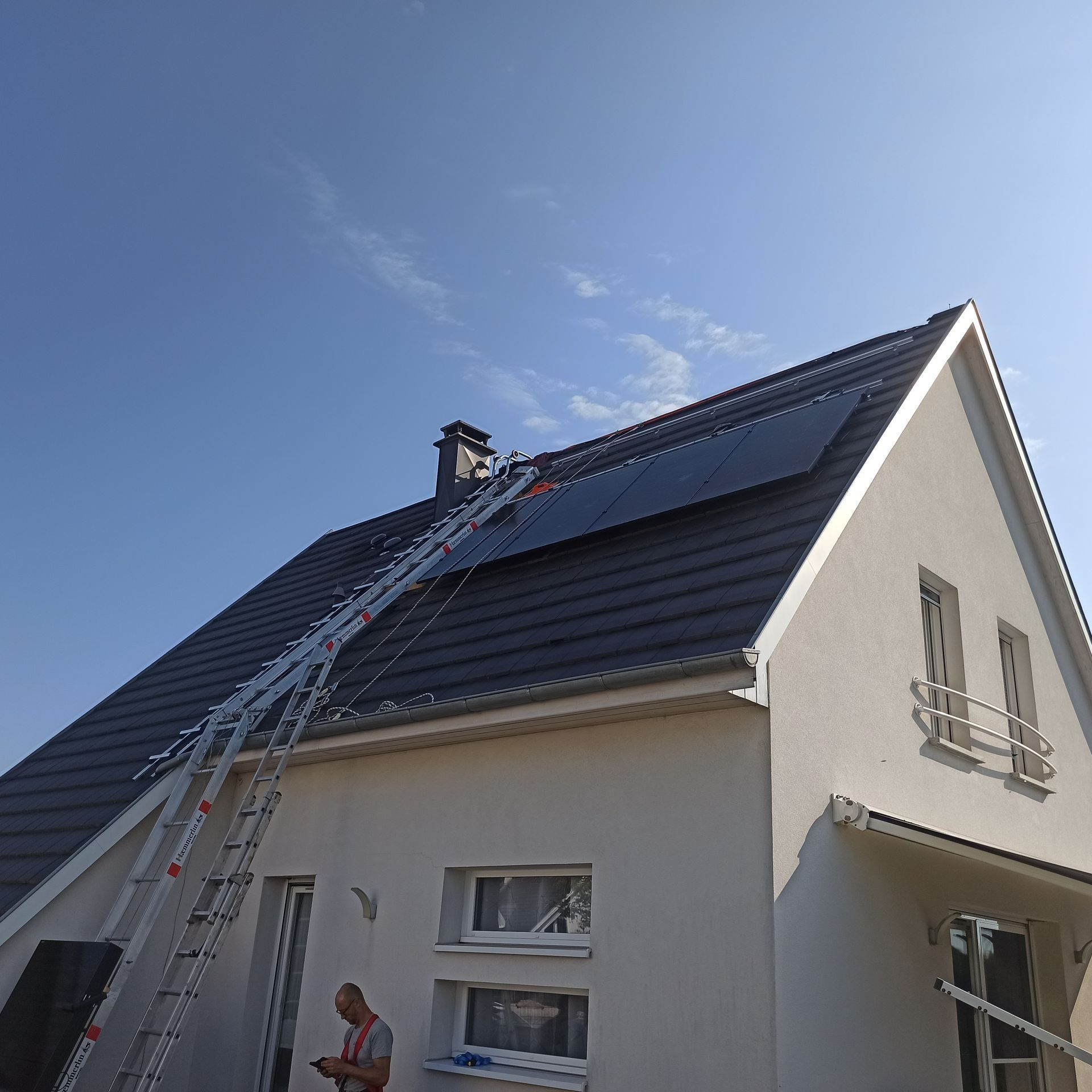 Maison avec panneaux photovoltaïques sur le toit, ouvrier sur une échelle, ciel bleu.