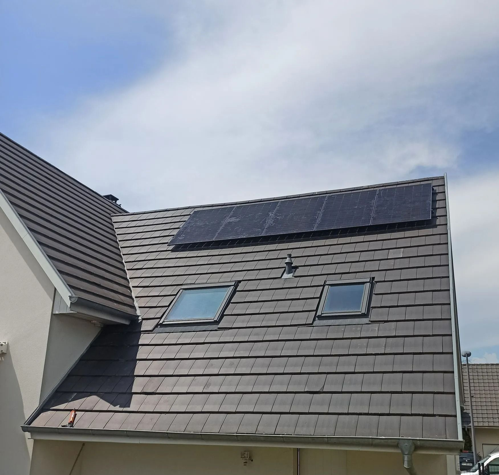 Panneaux photovoltaïques sur un toit de tuiles percé de deux puits de lumière.