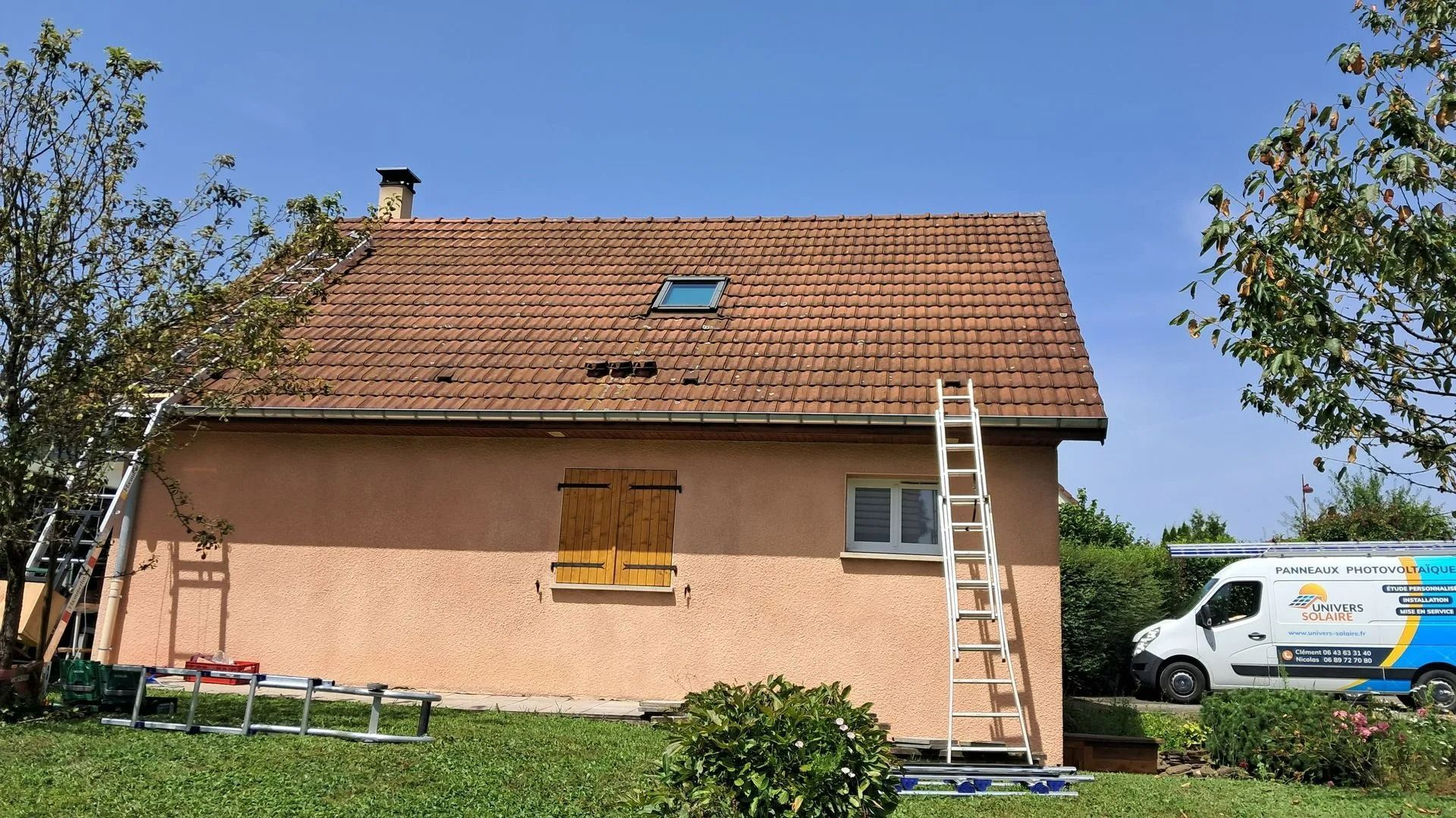 Maison au toit de tuiles brunes, échelles et camionnette.