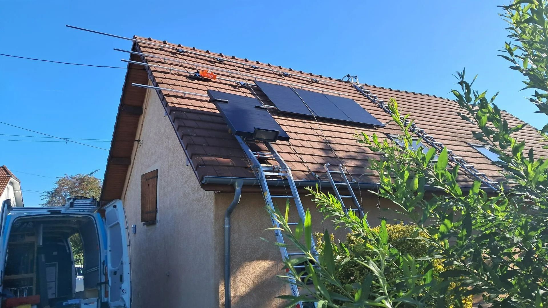 Panneaux photovoltaïques installés sur le toit d'une maison, échelle dépliée, camionnette garée en dessous.
