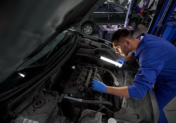 Un hombre está trabajando en el motor de un coche en un garaje.