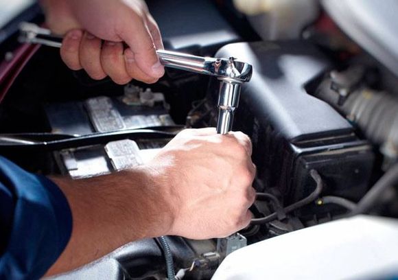 Un hombre está trabajando en el motor de un automóvil con una llave inglesa.