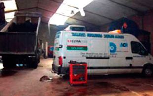 Una camioneta blanca está estacionada en un garaje al lado de un camión volquete.