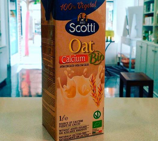 Un envase de bebida de avena con calcio Scotti sobre una mesa, con el interior de una tienda ligeramente borroso al fondo.