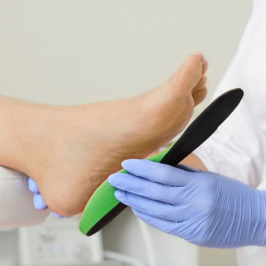 Un operatore sanitario con indosso guanti blu tiene una soletta ortopedica verde e nera contro il piede di un paziente.
