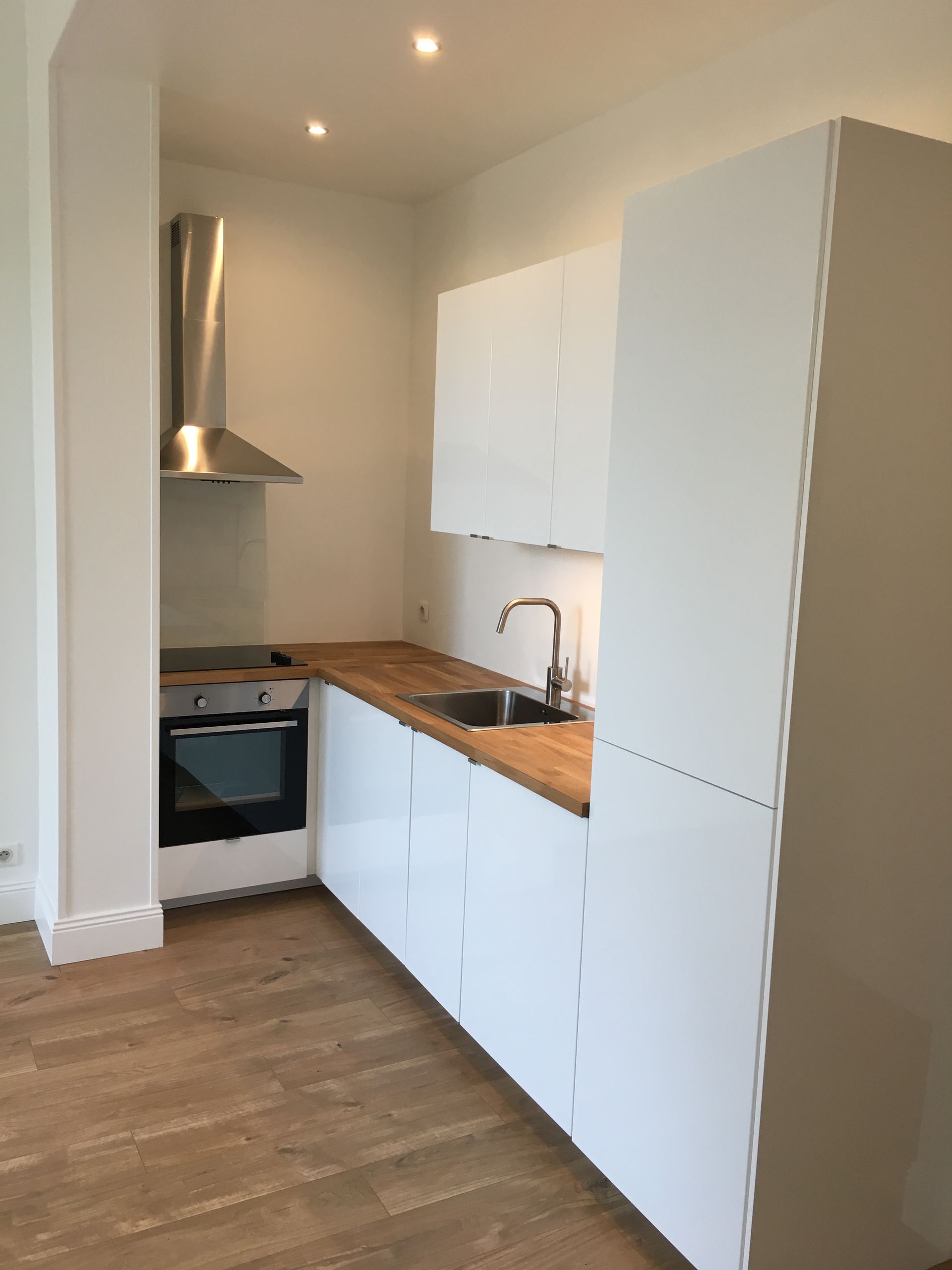 Petite cuisine blanche avec plan de travail en bois, hotte en inox et four.