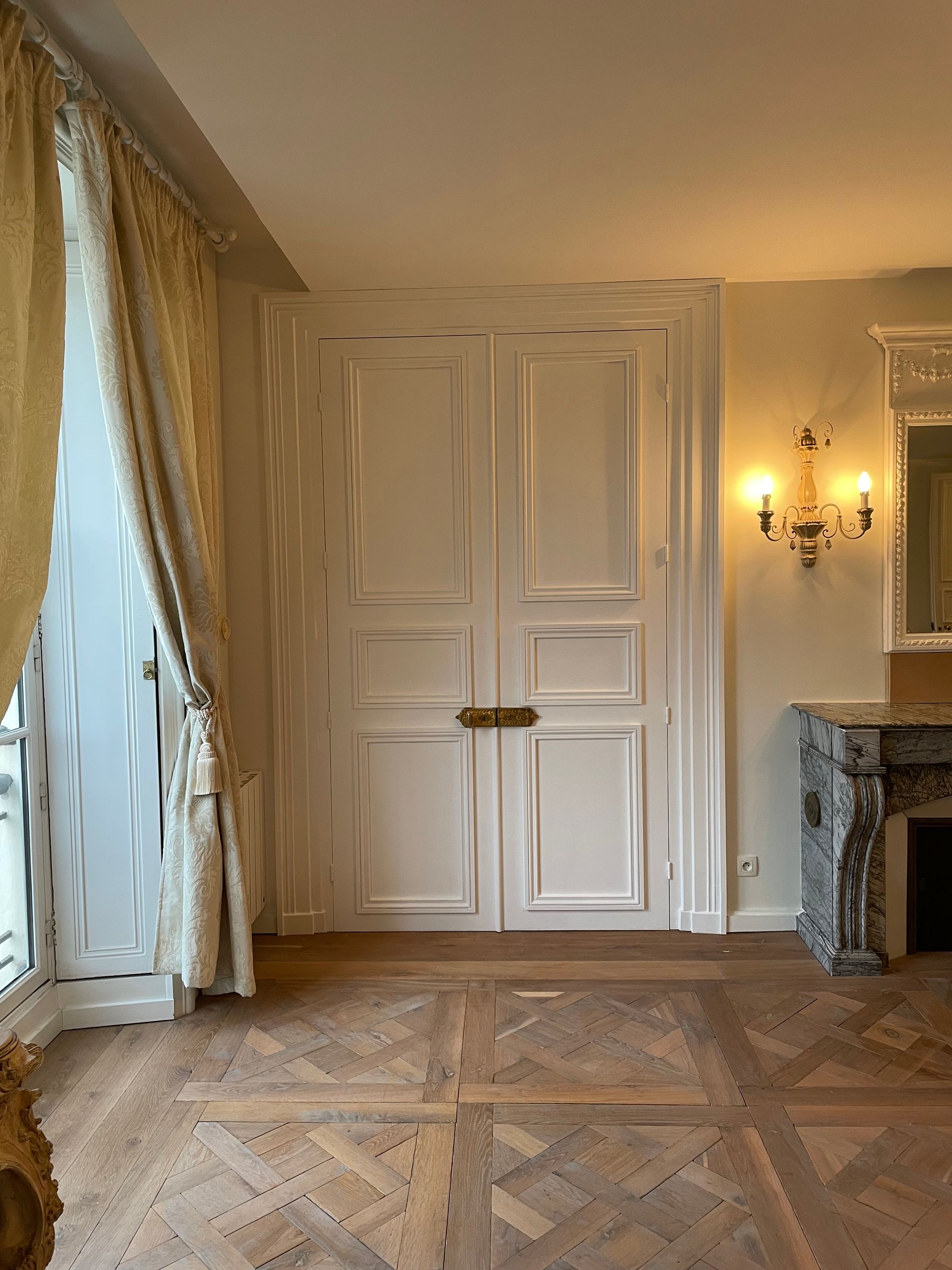 Portes doubles blanches et parquet dans une pièce avec cheminée et rideaux.