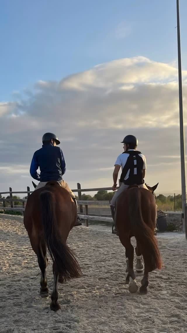 Dos personas montando a caballo en un camino de arena, contra un cielo nublado.