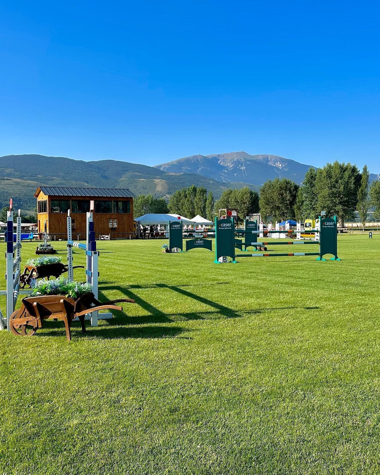 Recorrido ecuestre en un campo de hierba con montañas al fondo en un día soleado.