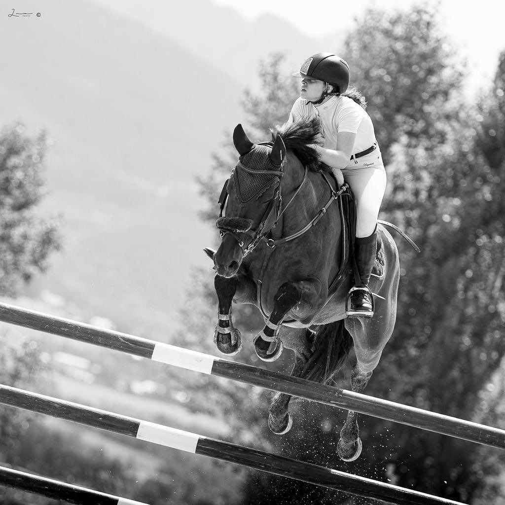 Mujer a caballo saltando una valla en una competición ecuestre. Blanco y negro.