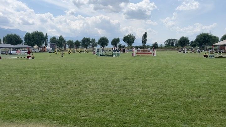 Un campo de hierba con saltos ecuestres. Jinetes y espectadores están presentes.