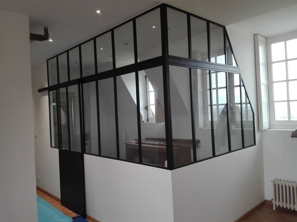 Cloison vitrée à cadre noir dans une pièce blanche lumineuse avec des fenêtres et un radiateur.