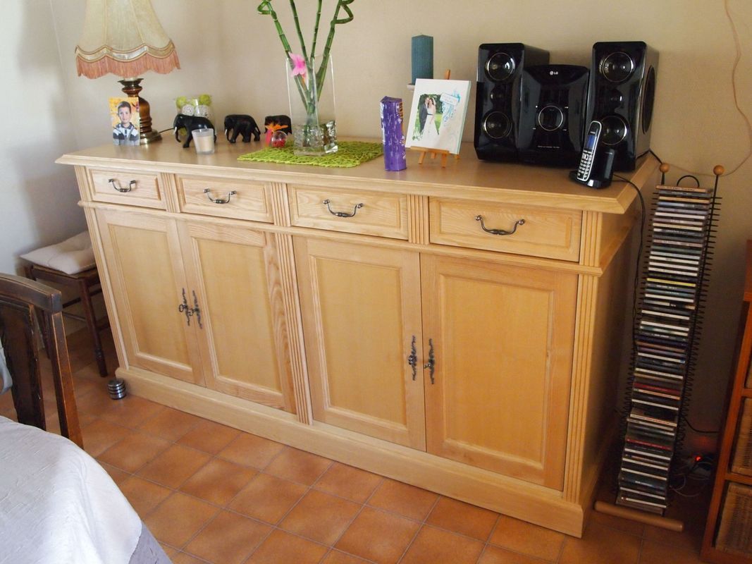 Buffet en bois avec des objets de décoration, une chaîne Hi-Fi et des CD contre un mur dans une pièce carrelée.