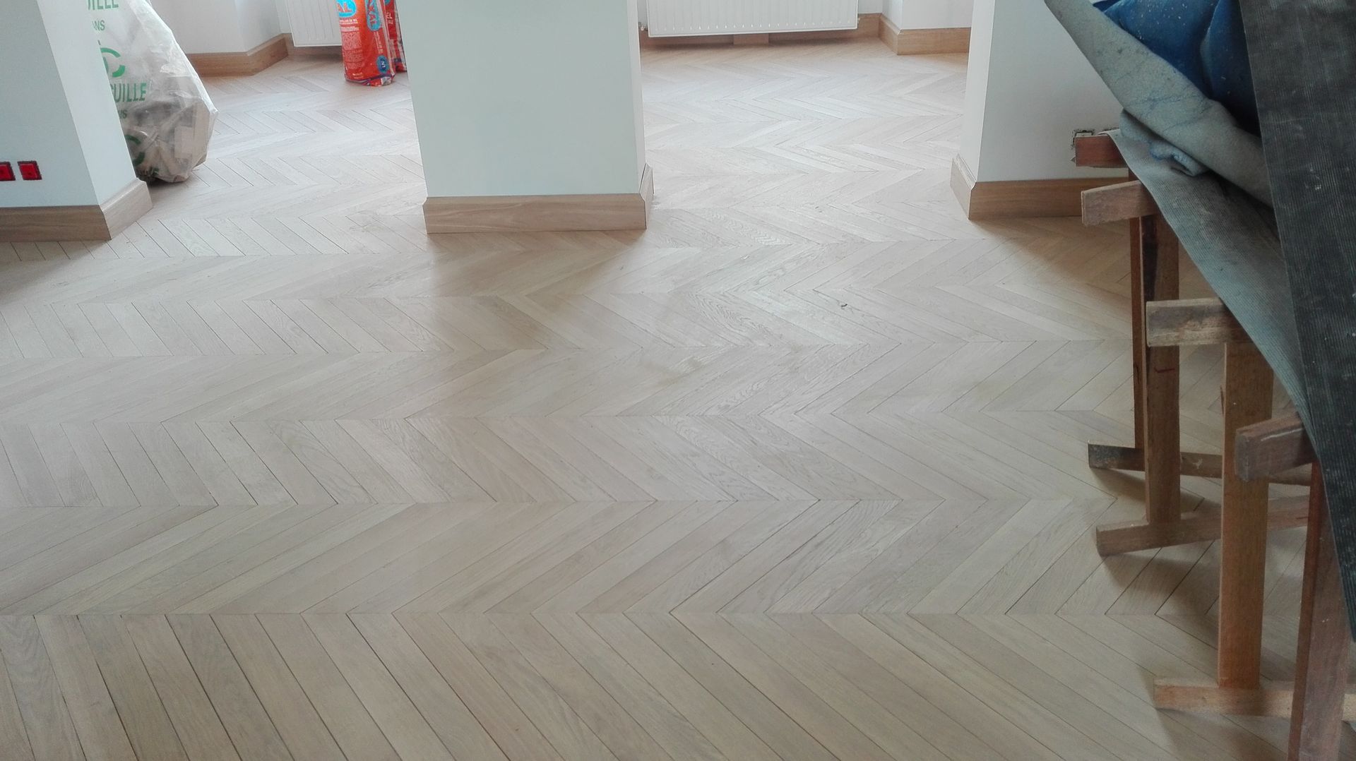 Un parquet en bois clair dans une pièce avec des colonnes blanches, une chaise et le bord d'un canapé visible.