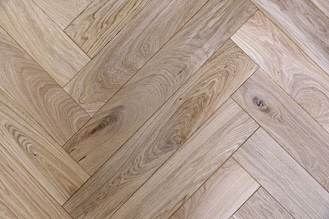 Parquet en bois clair à chevrons avec un veinage et des nœuds naturels.