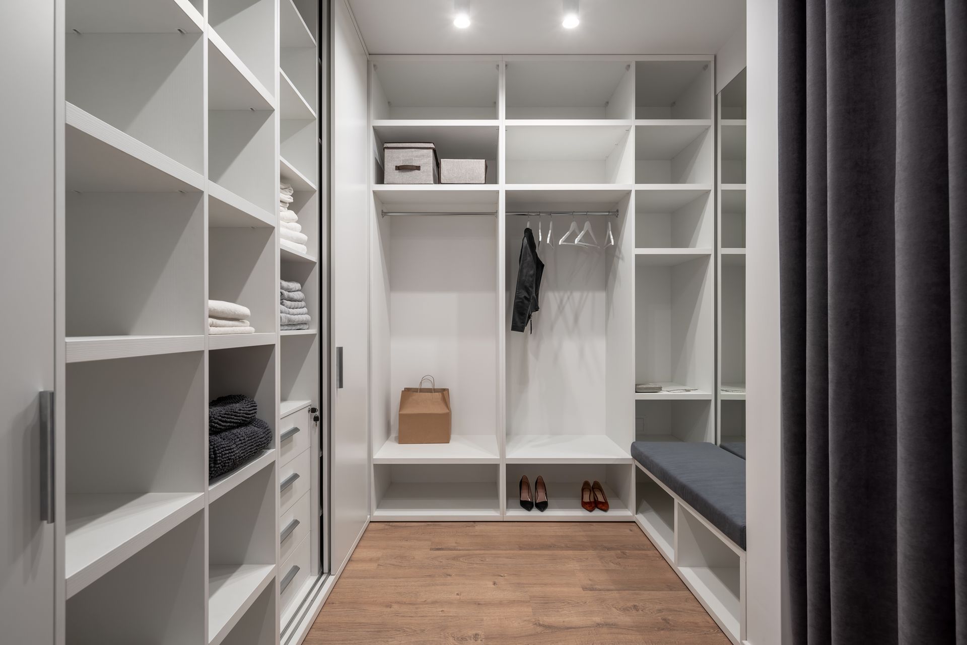 Dressing avec étagères blanches, vêtements suspendus, panier en osier, banc et parquet.