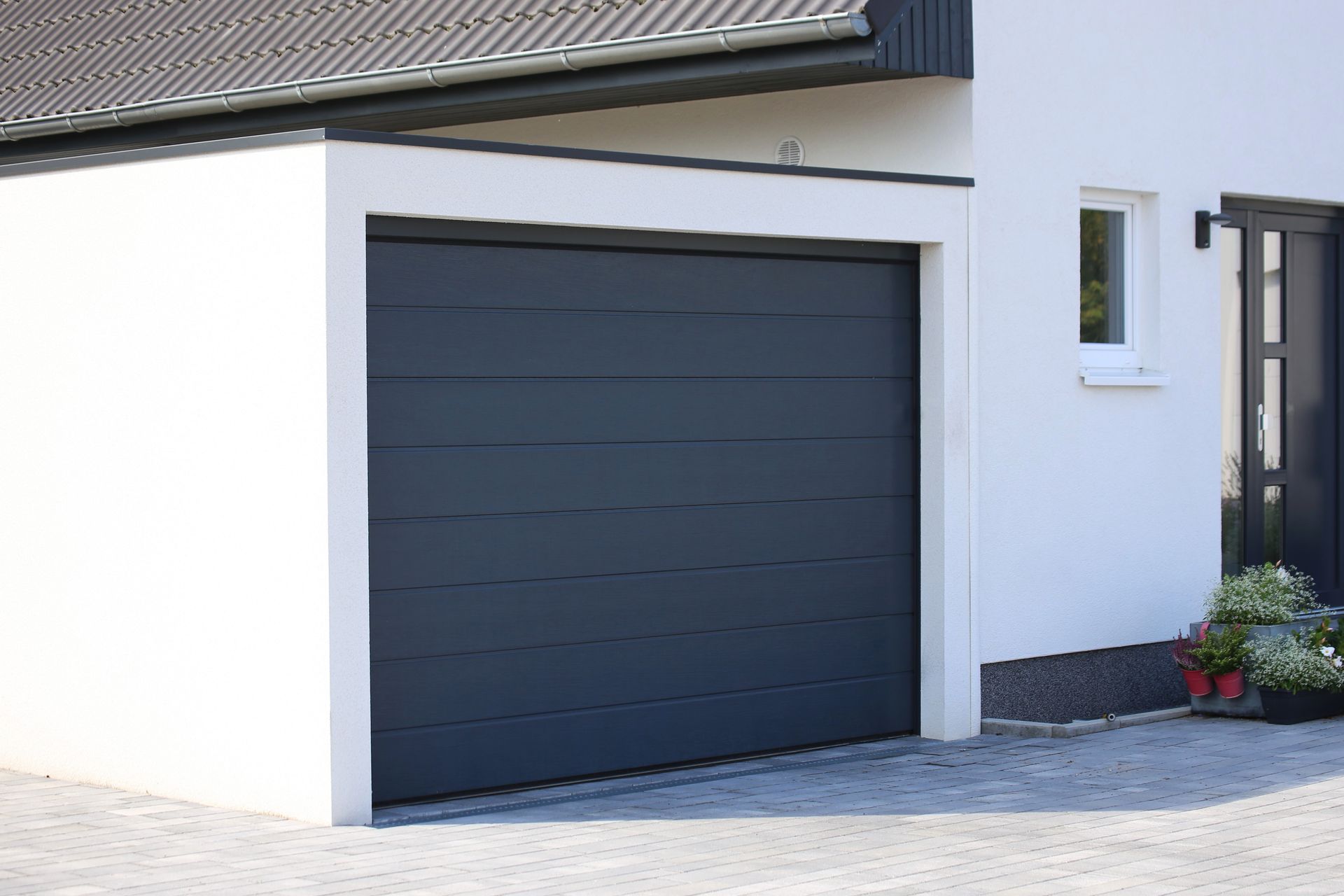 Maison moderne blanche avec une porte de garage bleu foncé et un petit jardin à l'avant.