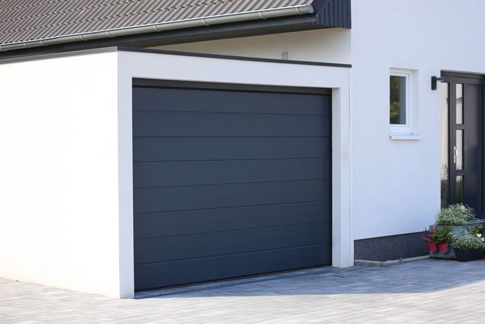 Extérieur de maison moderne avec une porte de garage gris foncé et des murs blancs.