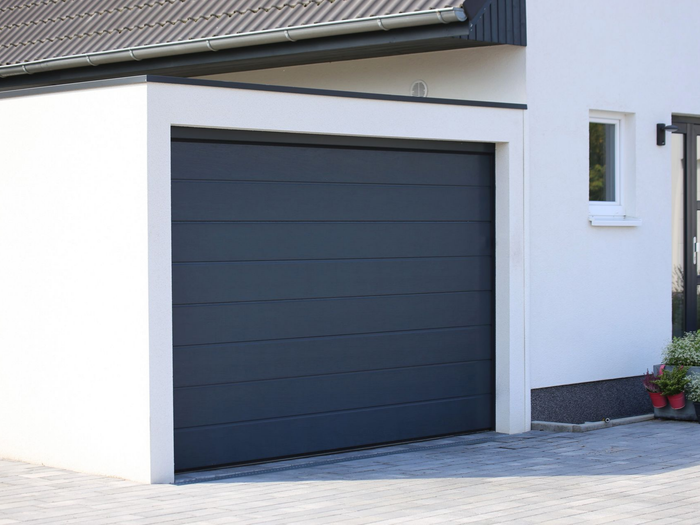 Extérieur de maison moderne avec une porte de garage gris foncé et des murs blancs.