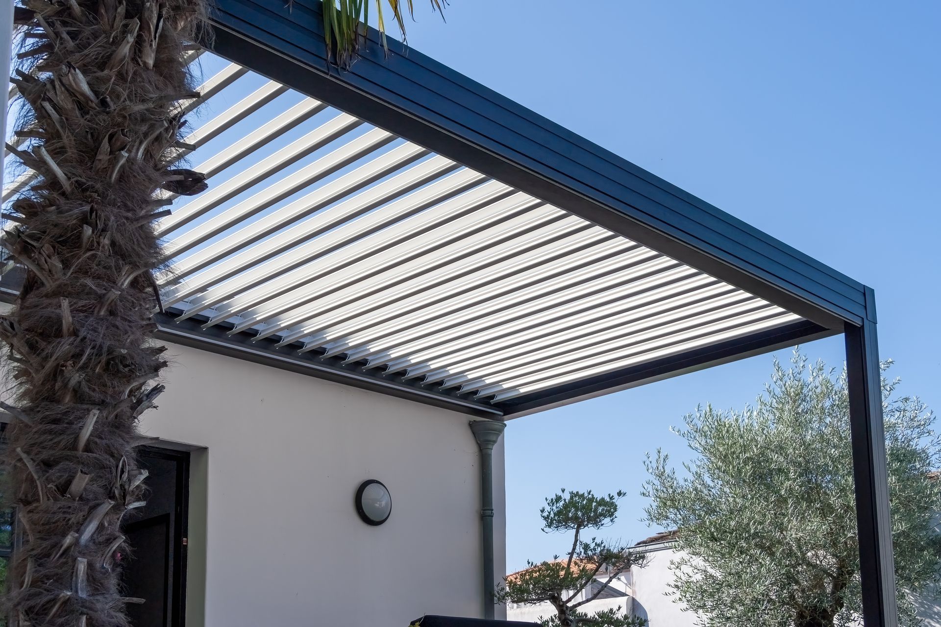 Pergola de patio moderne avec toit à claire-voie à côté d'une maison blanche et d'un palmier.