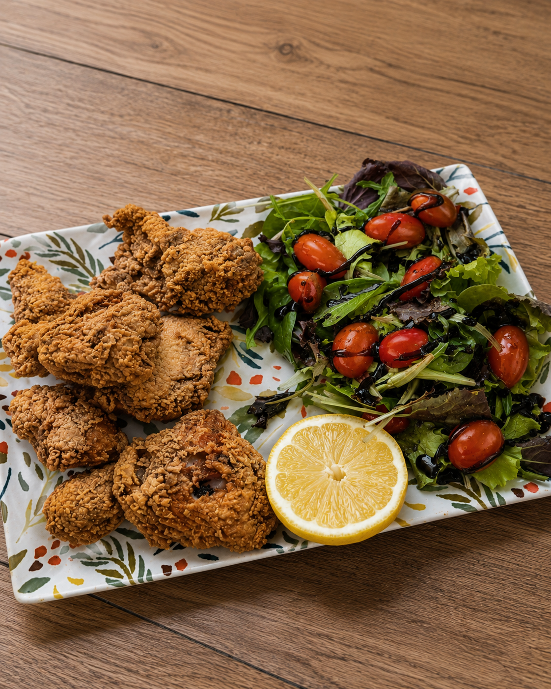 Pollo frito y una ensalada de hojas verdes con tomates cherry y limón en un plato estampado.