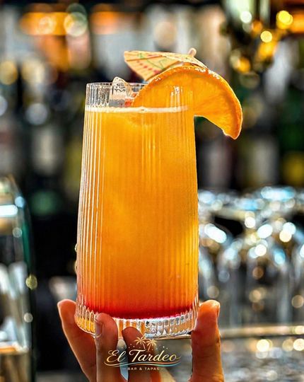 Cóctel alto de naranja con guarnición de cítricos en la barra.
