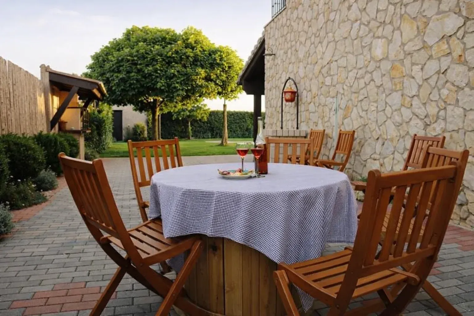 Mesa de comedor al aire libre con sillas, en un patio con paredes de piedra, con mantel a cuadros.